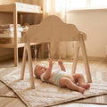Baby lying on a rug next to a wooden baby gym in a room with toys and books.