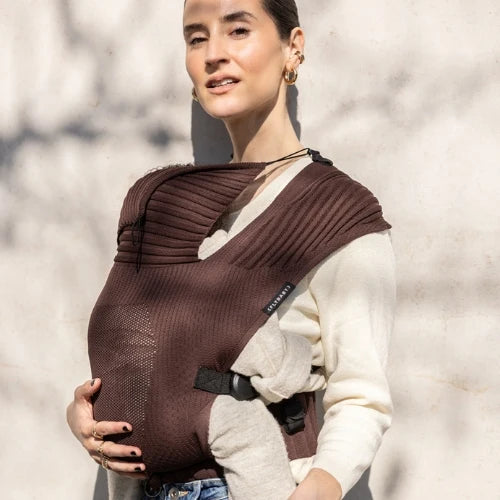 Person wearing a brown flybaby baby carrier against a light background