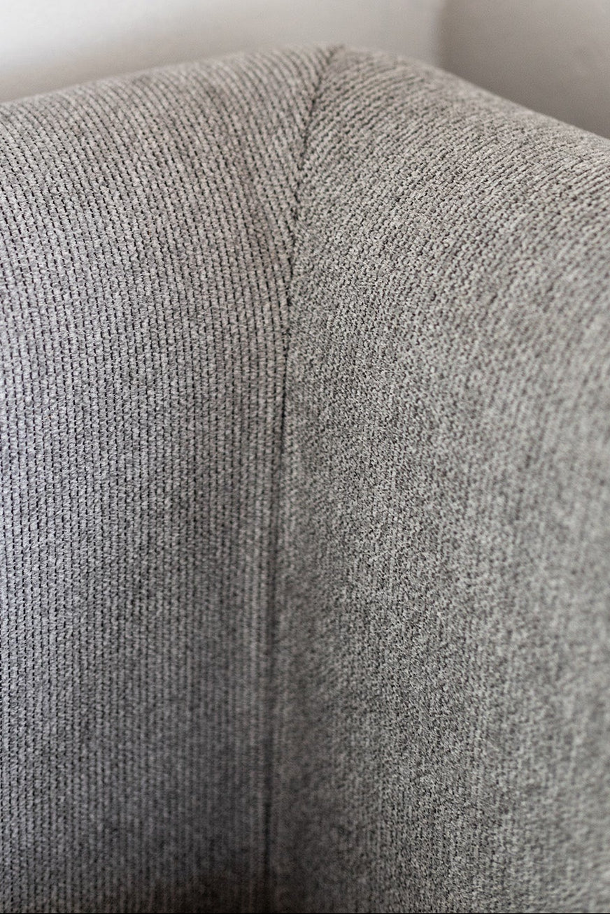Gray upholstered corner of a chair against a white wall