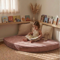 Child reading a book on a velvet cushioned reading nook with books and decor around.