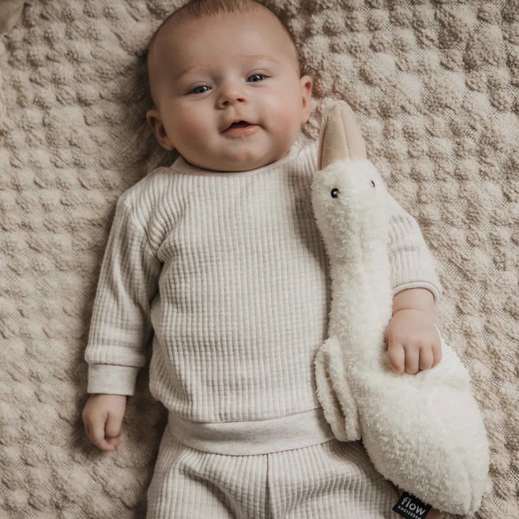 Baby in a white outfit holding a plush toy on a textured beige blanket