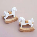 Two wooden rocking horses with white bodies on a beige background