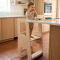 Child standing on a wooden step stool at a kitchen counter.