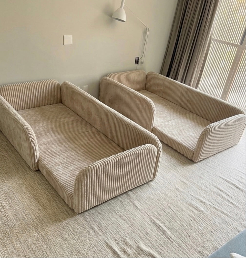 Two beige corduroy toddler bed bases in a room with a window and light fixture.