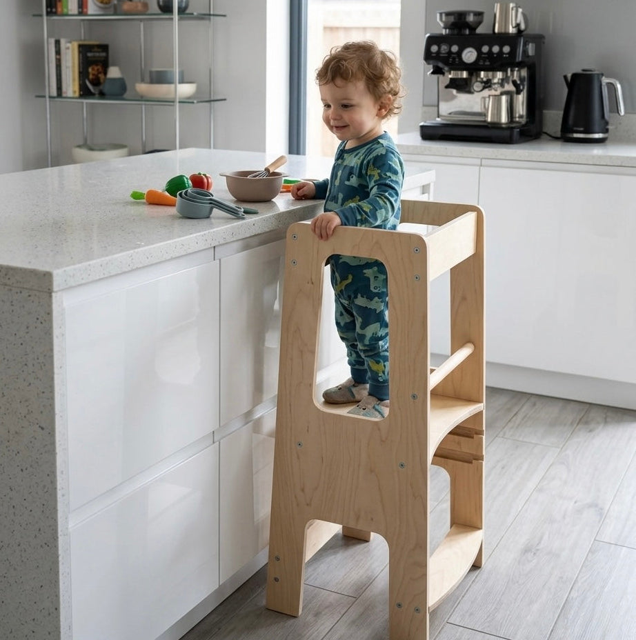 Child standing on a wooden step stool in a modern kitchen.