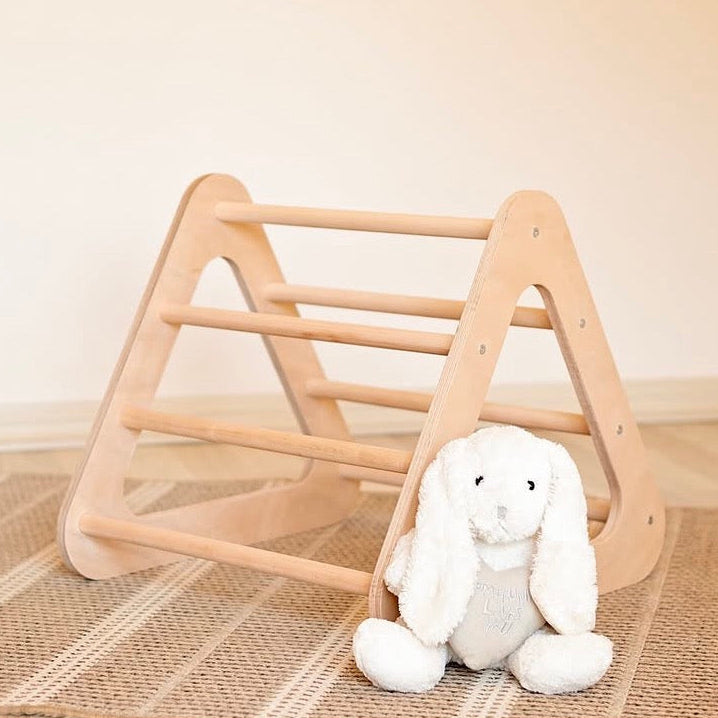 Wooden play gym triangle with a plush toy on a striped rug