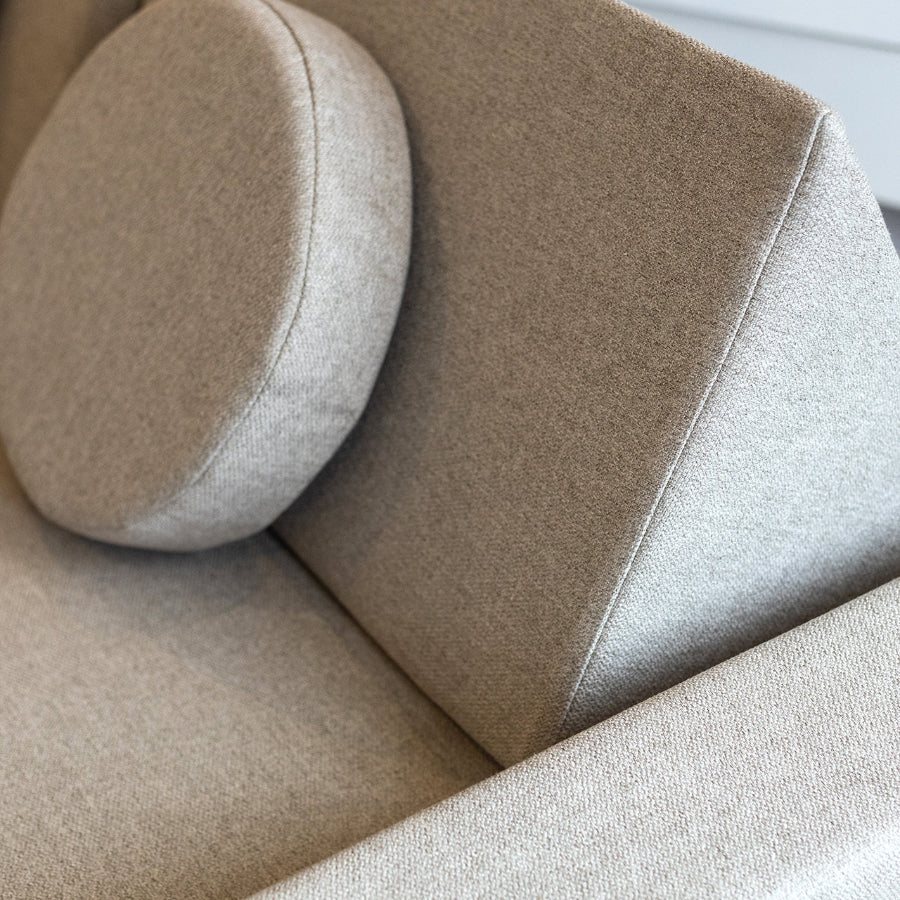 Close-up of a beige upholstered sofa with a matching round back cushion, showing the fabric texture and clean stitching.