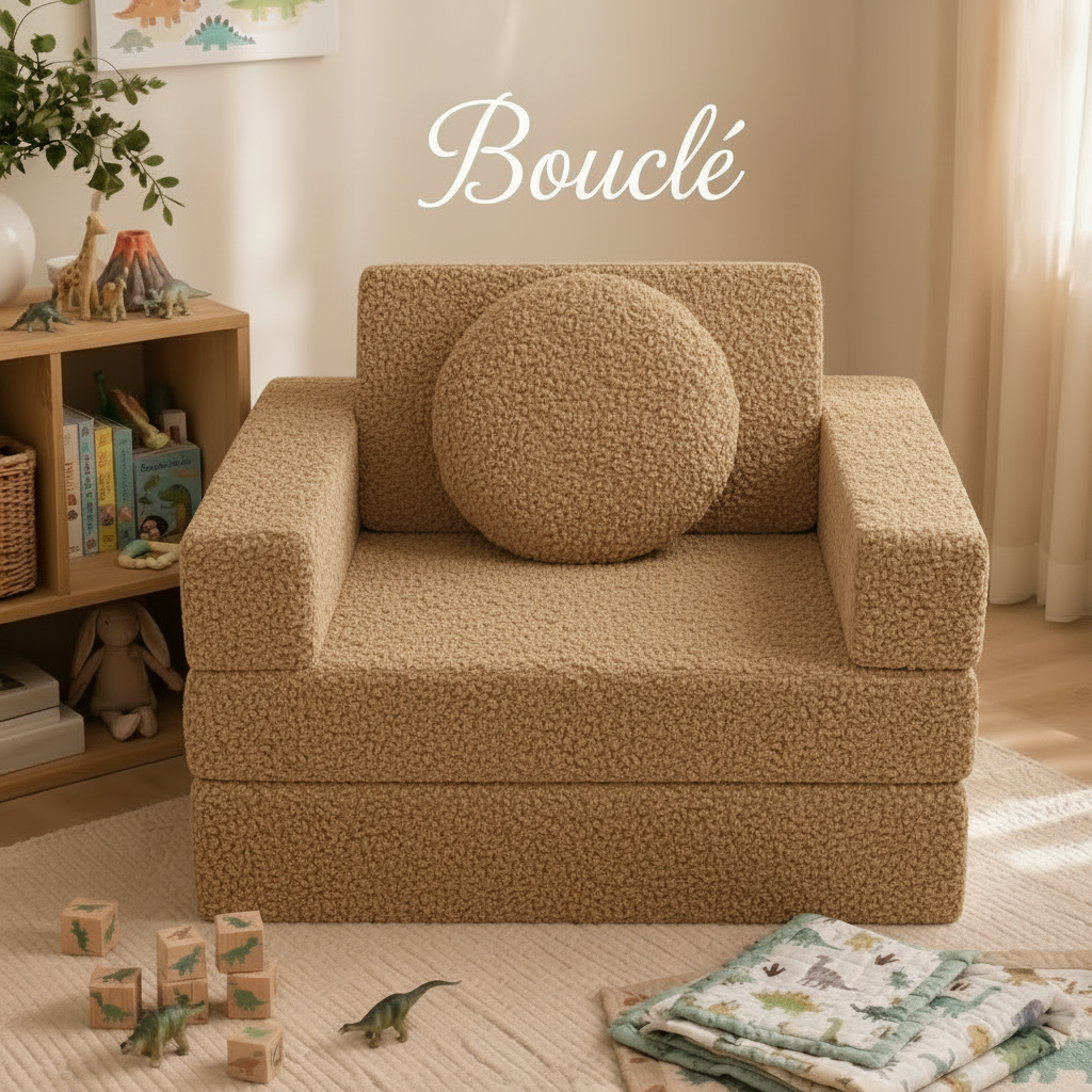 A beige bouclé upholstered children's armchair with a matching round throw pillow, shown in a styled nursery or playroom setting with toys, books, and a quilt on the floor. The word 'Bouclé' is written in script at the top.