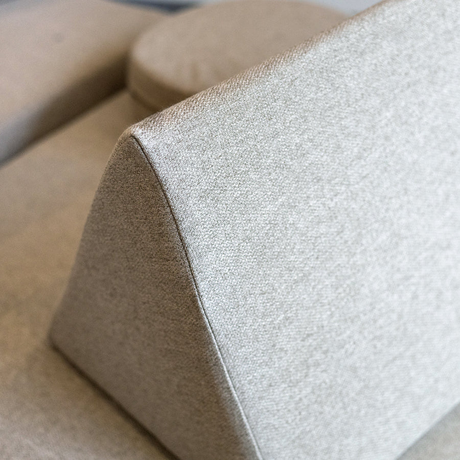 Close-up of a light beige textured fabric wedge pillow on a matching upholstered sofa.